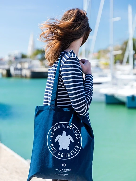 Femme portant un tote bag où est inscrit : la mer n'est pas une poubelle